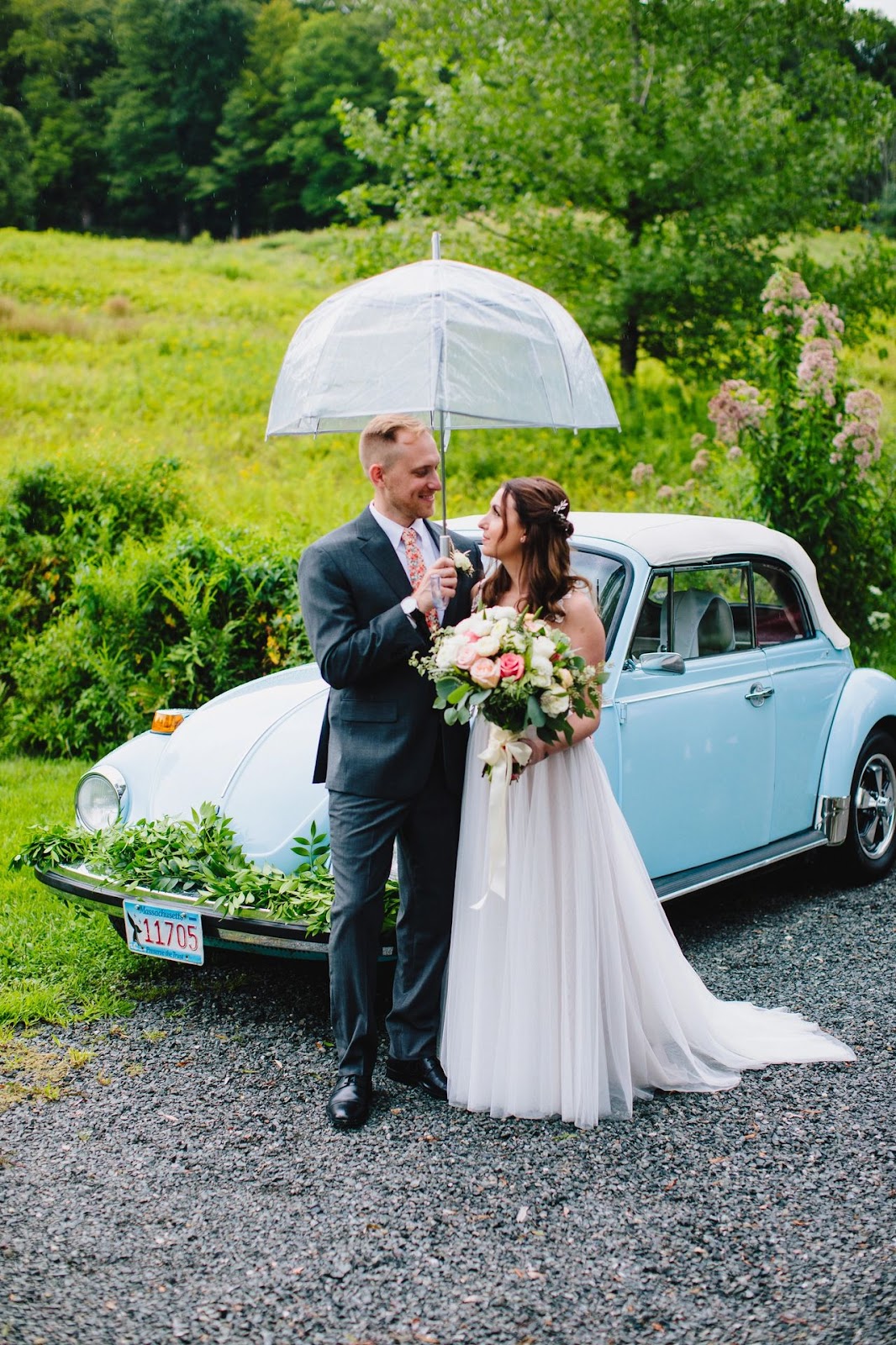 Bride and Groom under umbrella with a cool car behind them