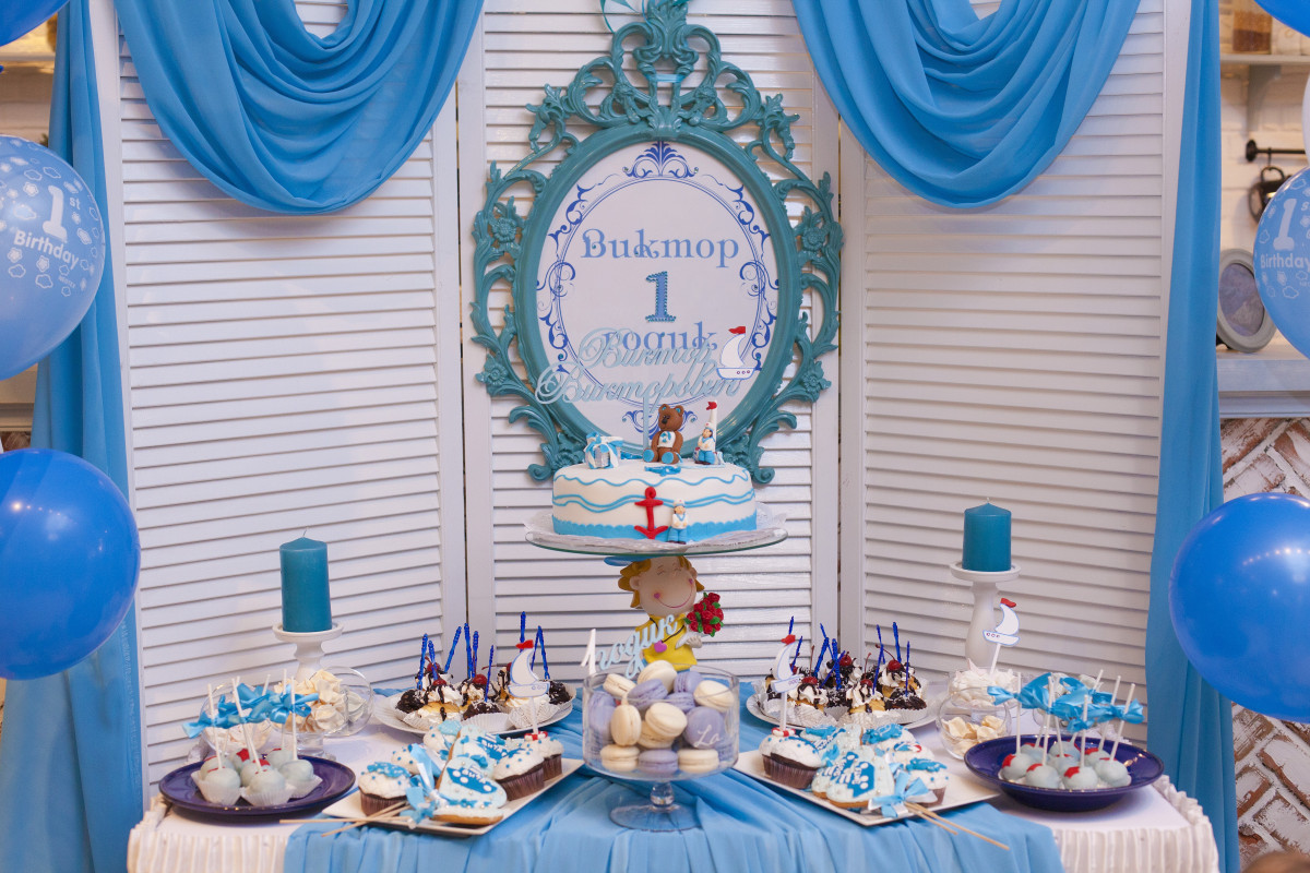 A festive scene featuring a white and blue-themed room adorned with sweet decorations, including a birthday cake with toppers, candles, and snacks that compliment the theme.