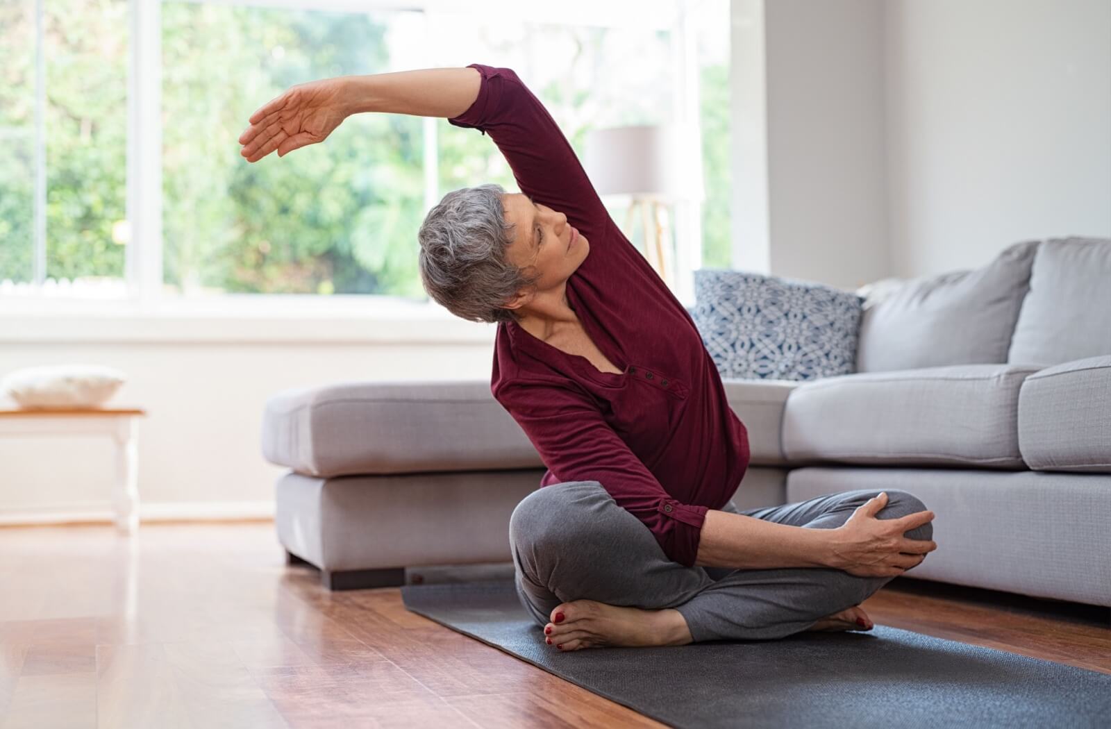 An older adult woman stretching while sitting on an exercise mat.