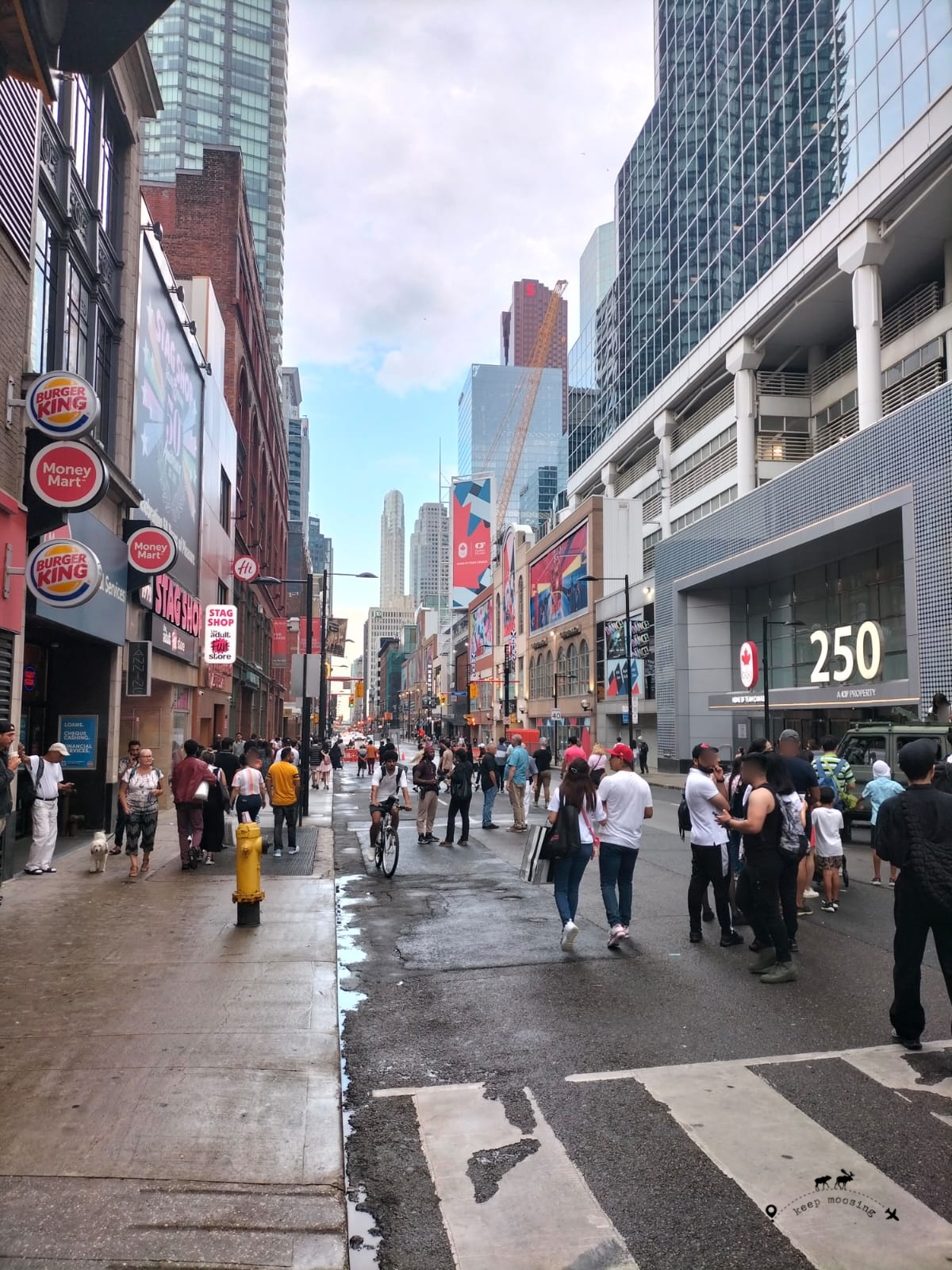 Crowded Yonge Street with the very tall skyscrapers of downtown Toronto on its sides.