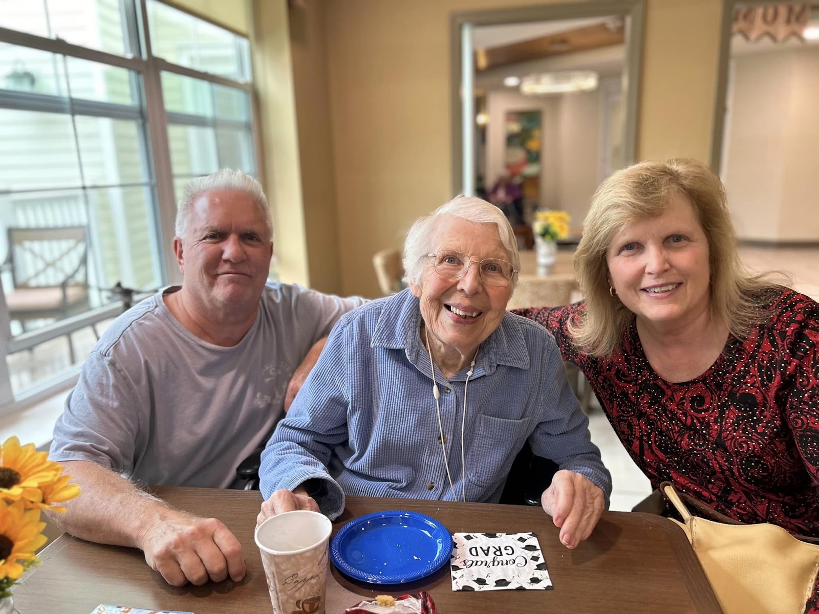 An elderly woman smiling while sitting at a table with family members