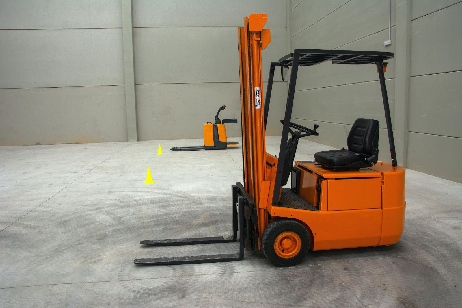 Two forklifts surrounded by yellow cones in an empty warehouse