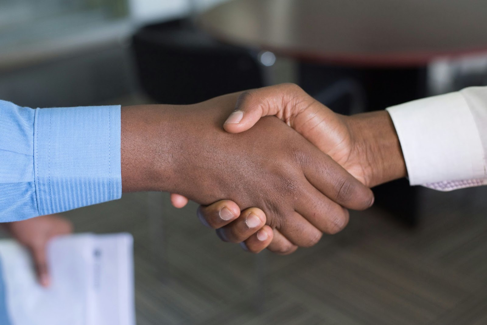 A close-up image of two hands shaking with a table in the background.