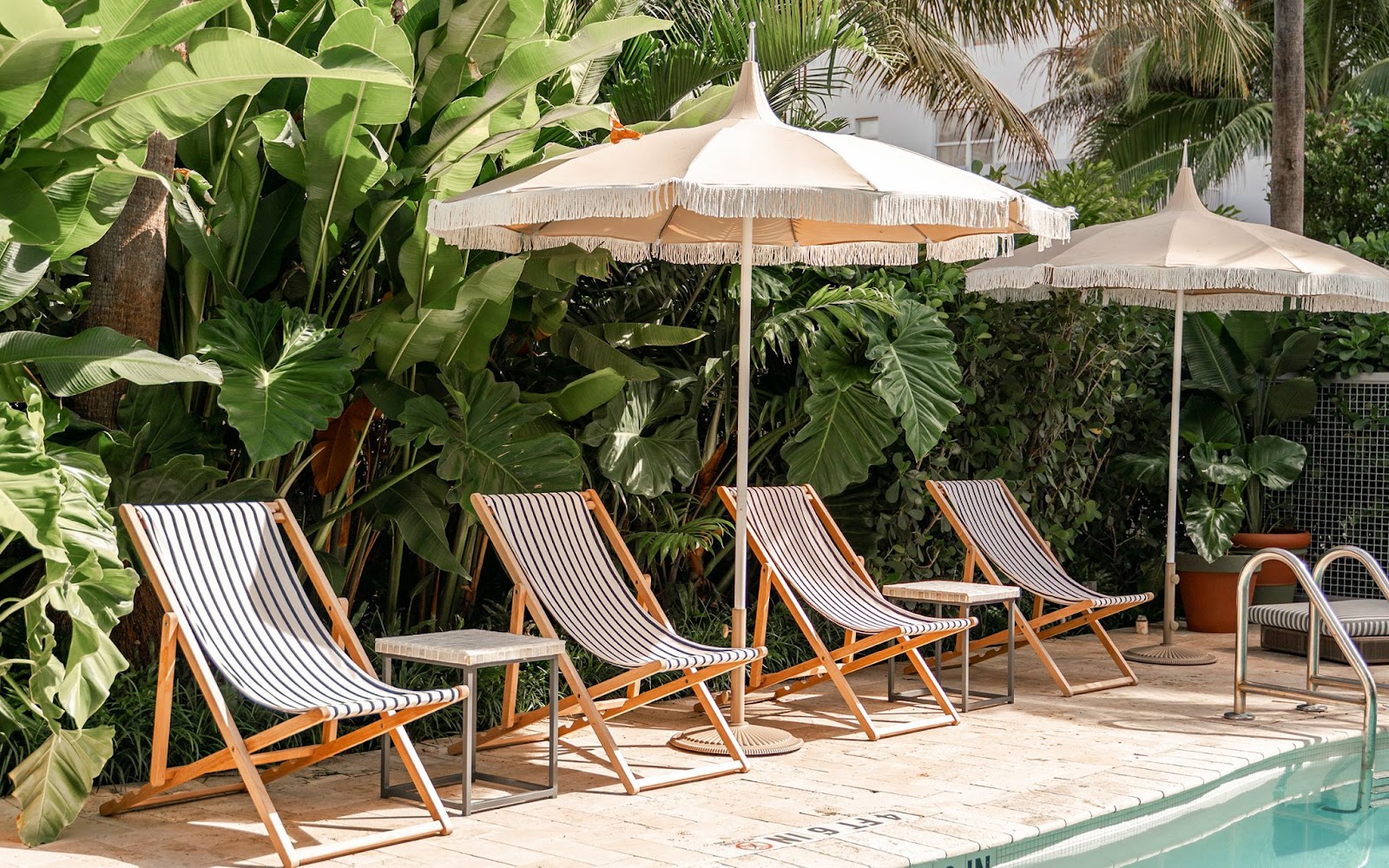wooden sling chairs set up by pool shaded by patio umbrellas