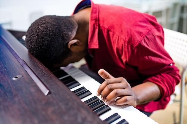 Upset african american handsome musician man discontent singing and teaching to play on piano