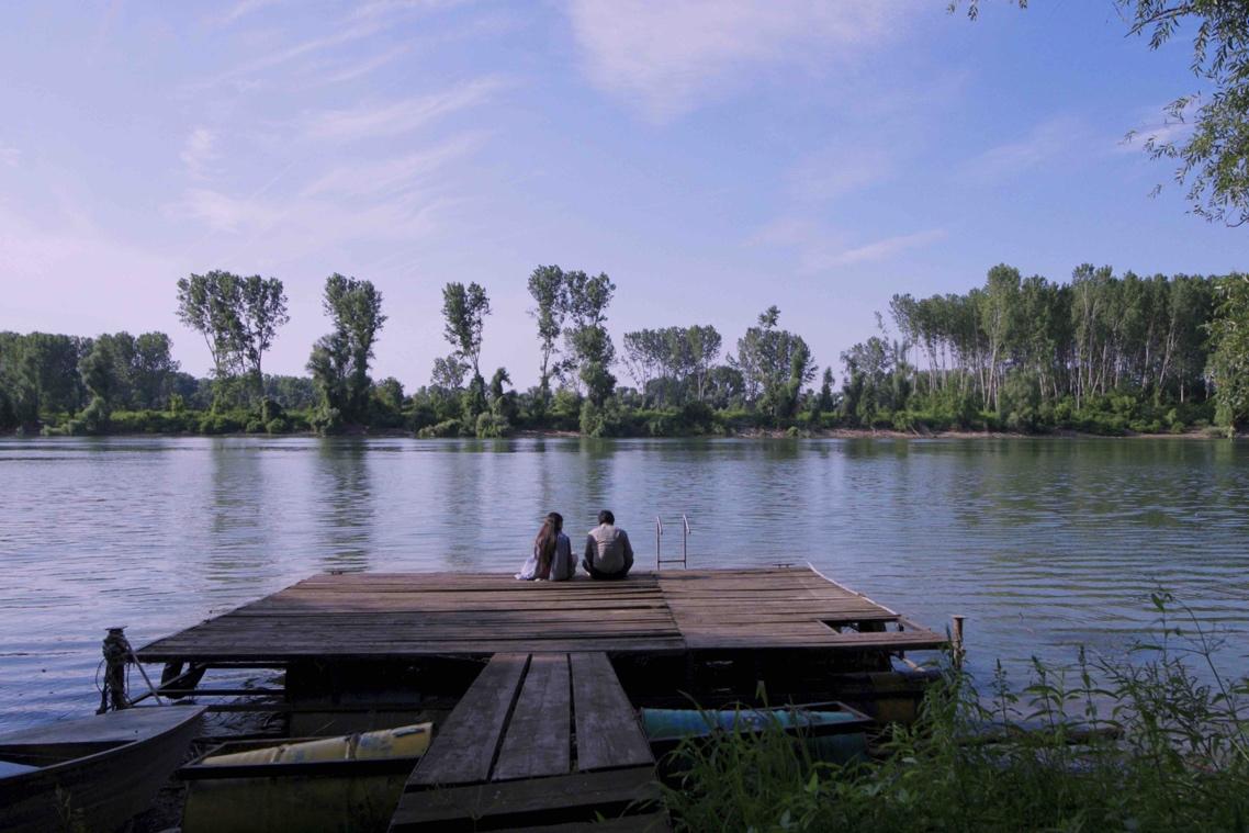 A couple sitting on a dock overlooking a lake

Description automatically generated