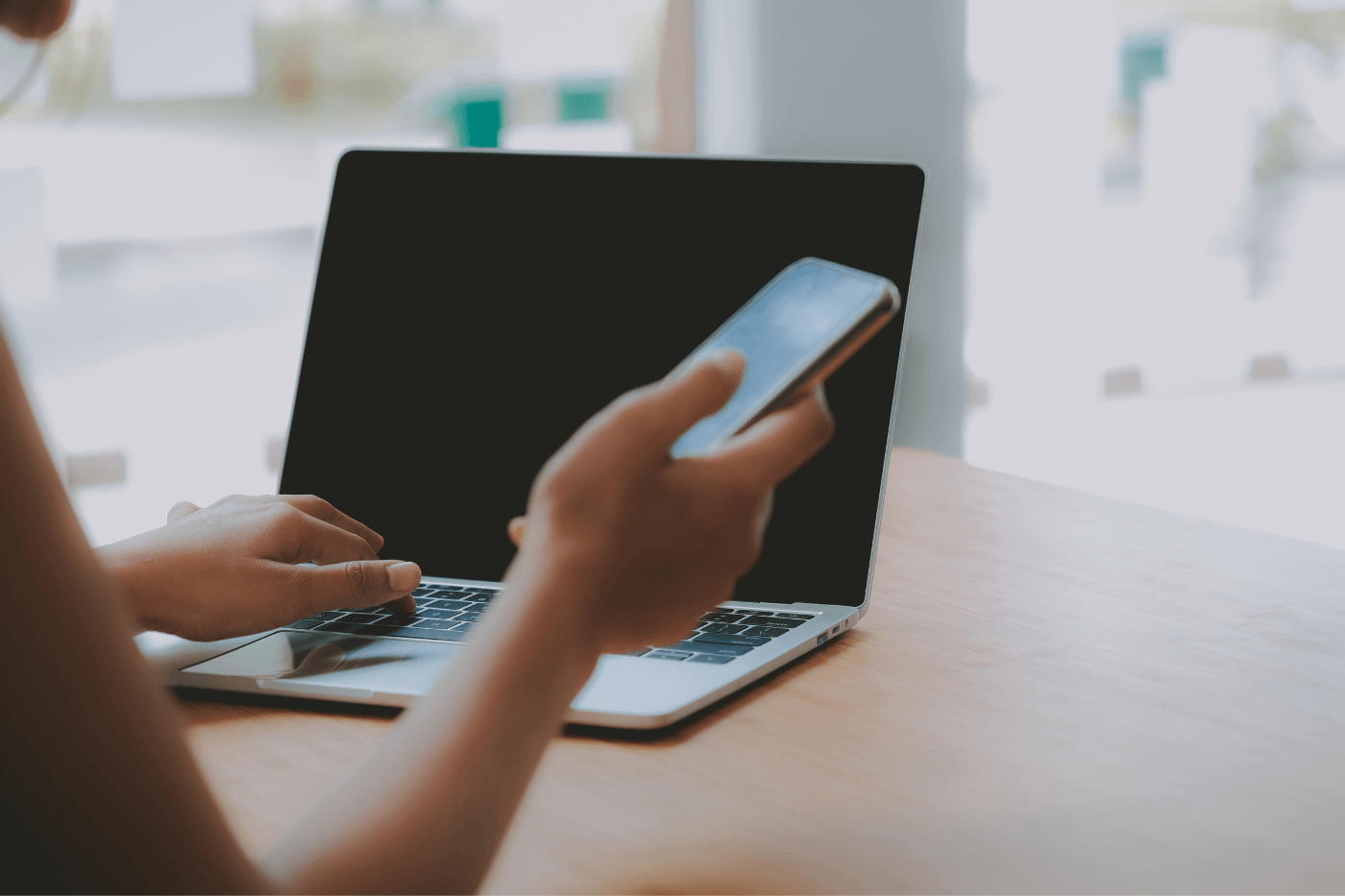 a woman holding her phone and typing on laptop