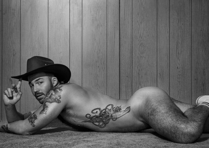 Dillon Cassidy posing naked on the rug while wearing a cowboy hat in black and white model shot