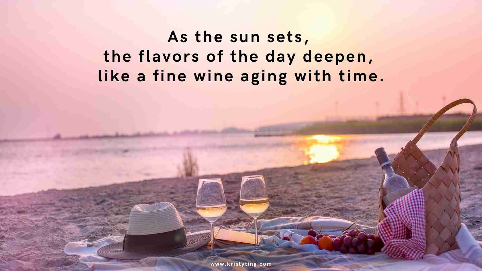 A beach picnic setup with a basket and glasses of wine at sunset.