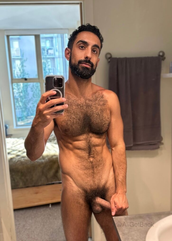 Ali Rush standing naked taking an iphone mirror selfie while pulling at his flaccid cock in the bathroom