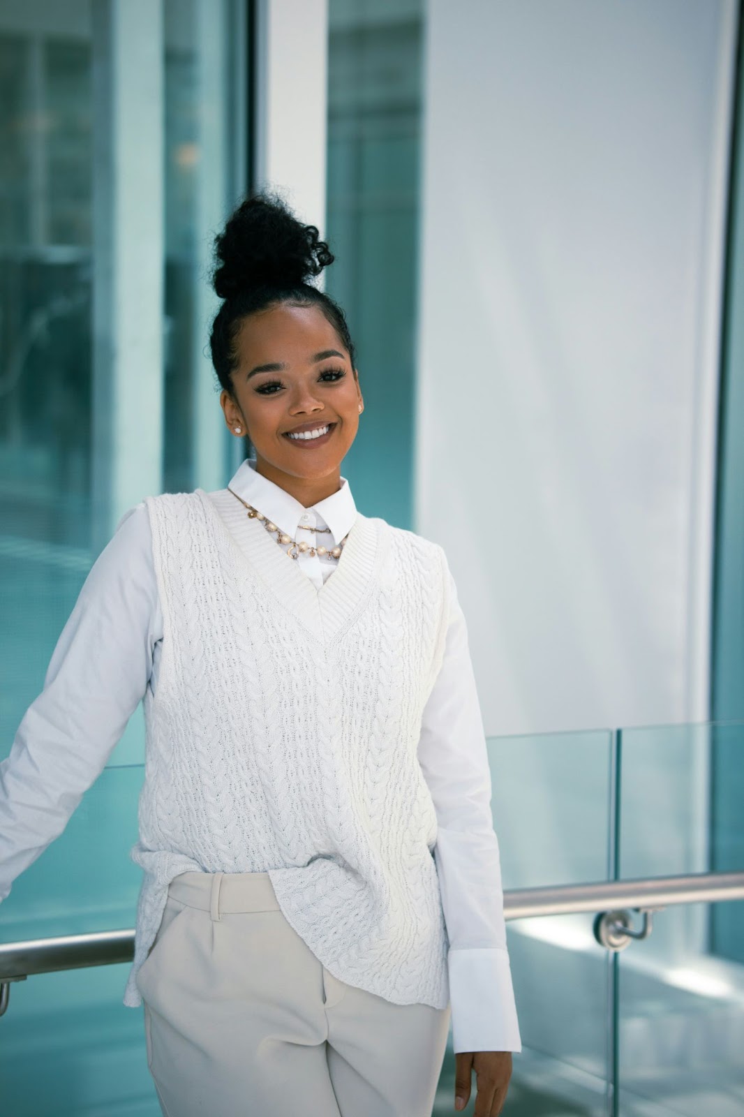 A woman in a classic white shirt and sweater paired with a beige trouser is posing for her realtor headshot.