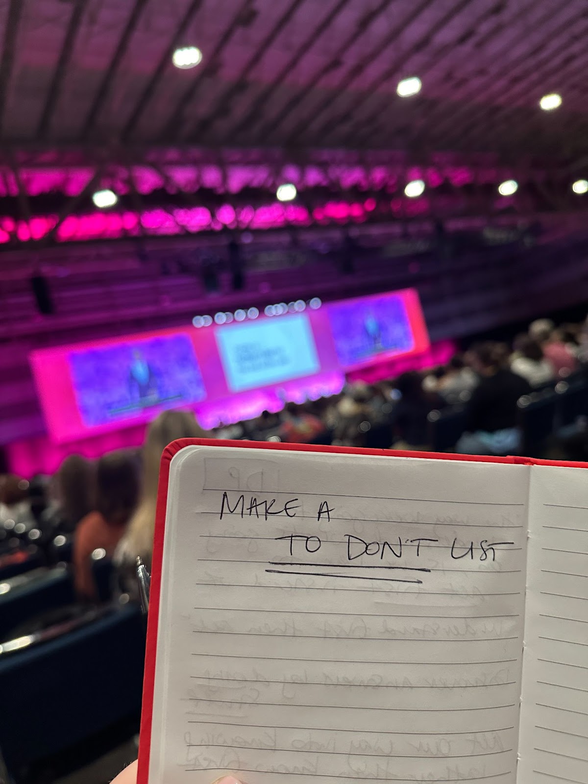 This is a picture of a notebook held up in front of the stage at a conference. The notebook has the words, "Make a To Don't List" written on it.