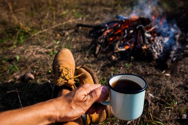 Free photo man holding a cup of coffee next to a campfire