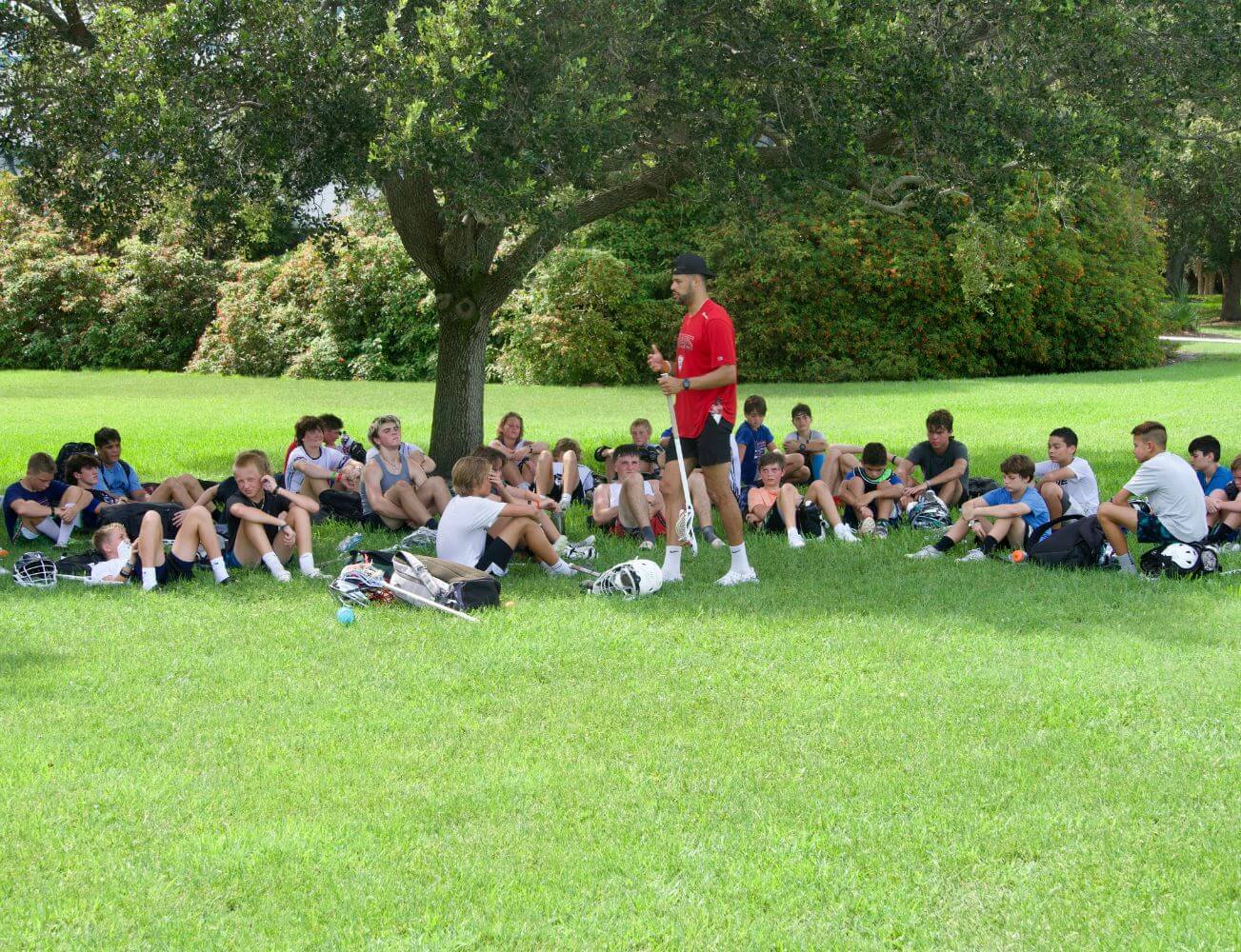 A group of young lacrosse players at summer sports camp listening as a coach talks to them