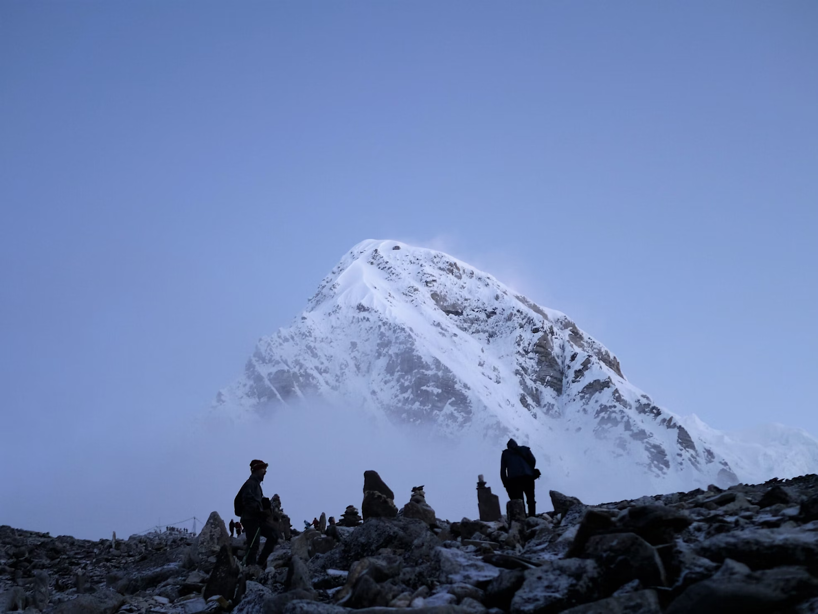 Silhouettes of trekkers ascending rocky terrain with snow-capped mountain in the background, symbolizing the Everest Base Camp Trek and Sherpa culture exploration.
