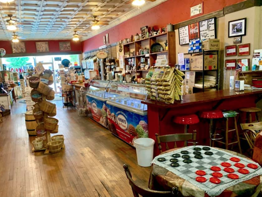 Image of the inside of the Wendell General Store. Wood floors, checkers game set up in the corner. Ice cream freezers for serving customers. 