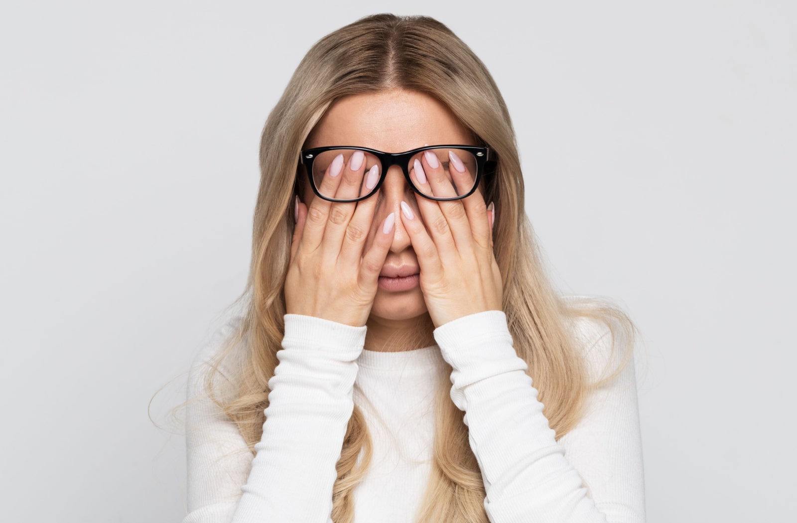 A woman holds both of her hands over her eyes and underneath her glasses due to eye strain