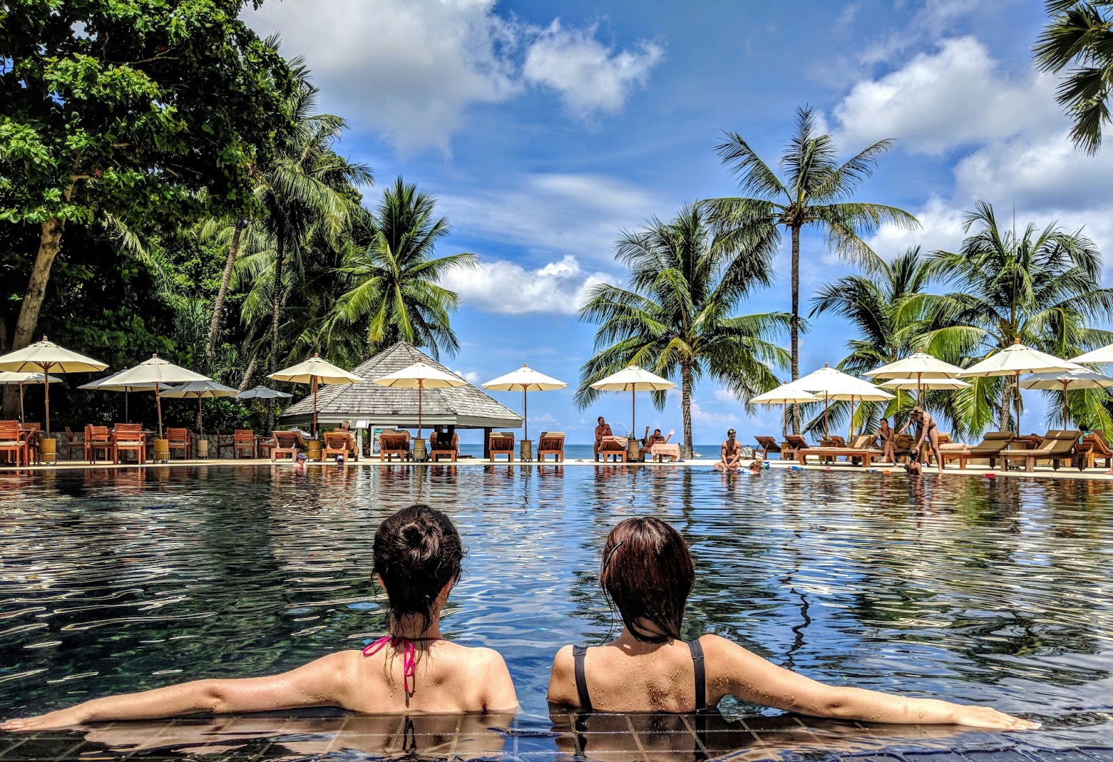 Wedding guests mingle by a shimmering pool, surrounded by lush tropical foliage at a luxury resort.