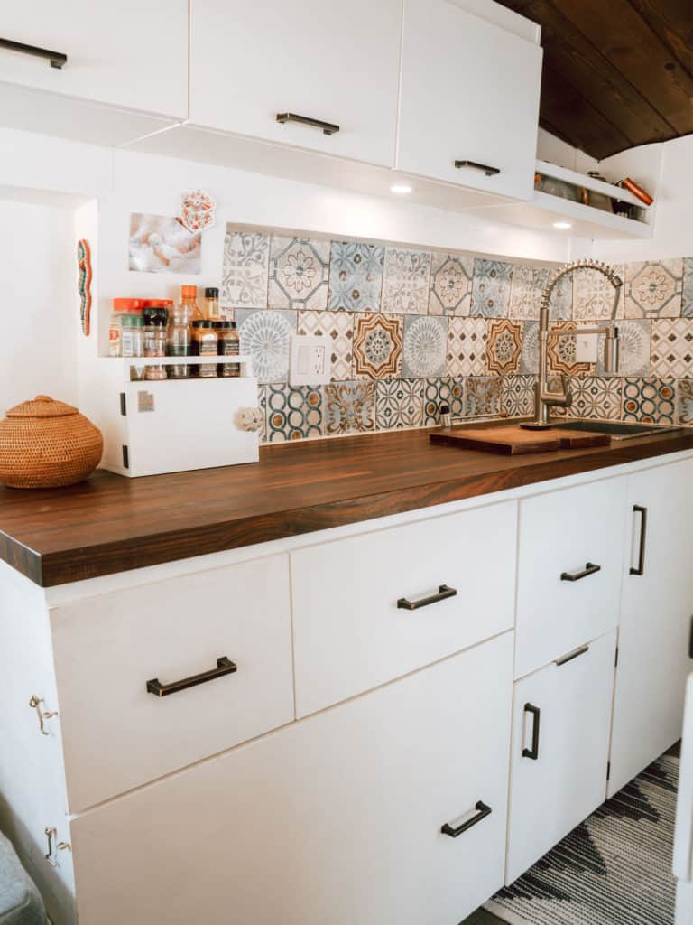 Camper van kitchen with counter, butcher block counter top, over head cabinets, and lighting