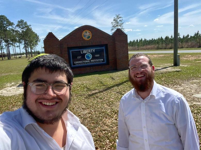 Two men standing in front of a sign

Description automatically generated