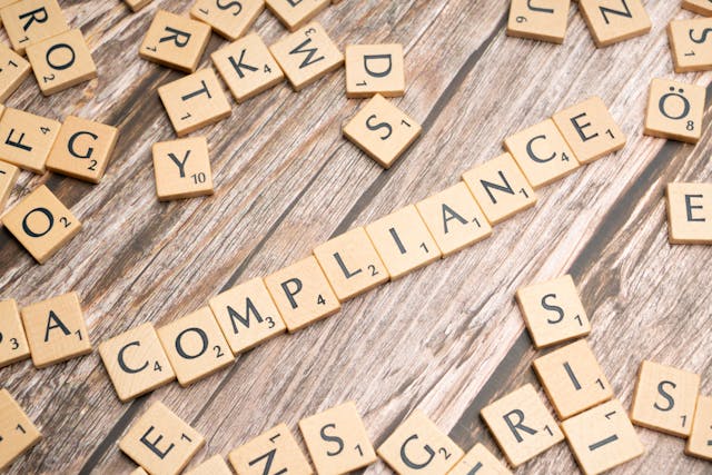 A pile of wooden tiles with letters on a table with the word Compliance