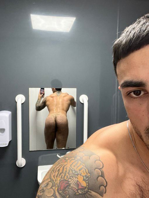 Nick_at_Night leaning naked in the gym bathroom taking a gay mirror selfie and showing off his hairy ass cheeks