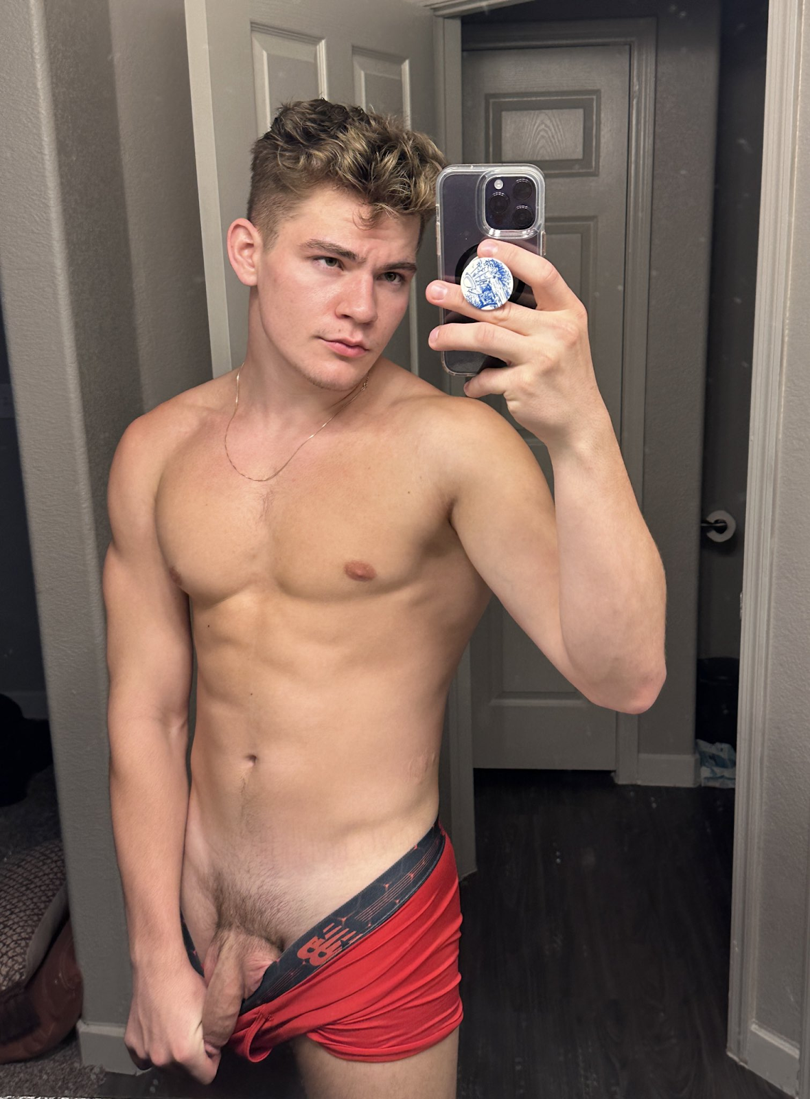 Oliver Marks standing in the bathroom mirror taking a selfie while pulling down his red undies and revealing his flaccid uncut cock