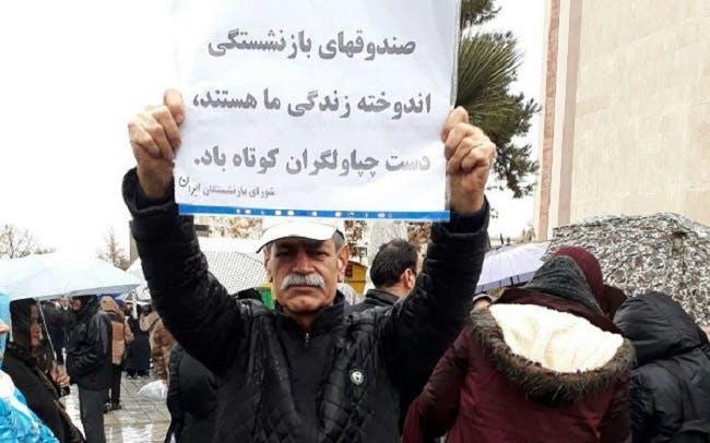 یک بازنشسته معترض کاغذی در دست دارد که بر آن نوشته است «صندوق‌های بازنشستگی اندوخته زندگی ما هستند. دست چپاولگران کوتاه باد»د