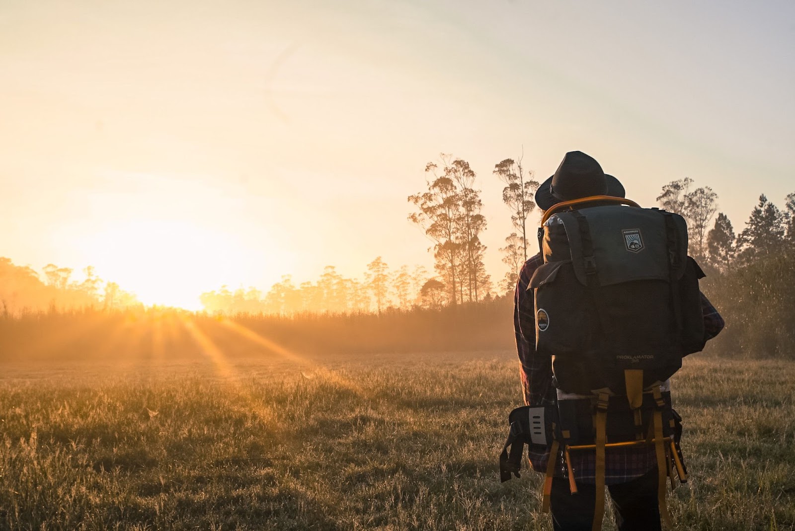 A guy wearing a hat and a backpack looking at the sunrise
