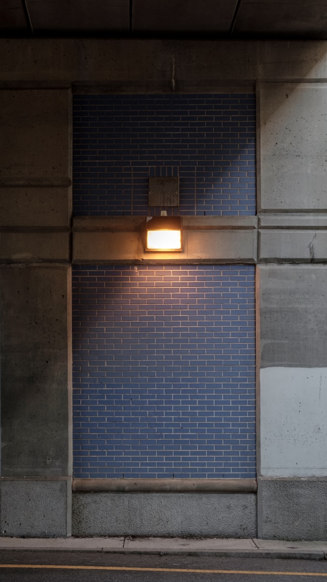 A wall with different textures including a blue brick wall accent and the rest is concrete with a halogen light on it