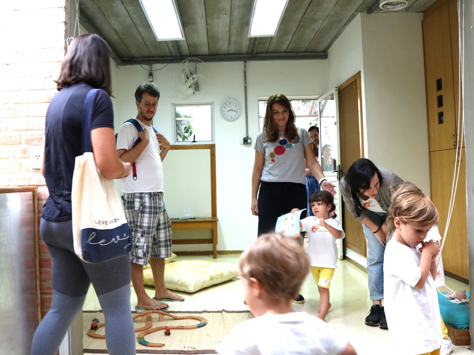 A imagem mostra uma sala com crianças e adultos.