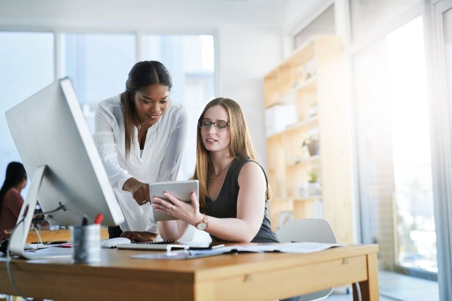 Two women collaborating on a computer in a professional office setting.