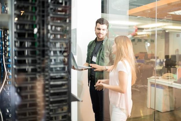 Free photo two business people standing in server room with laptop and discussing