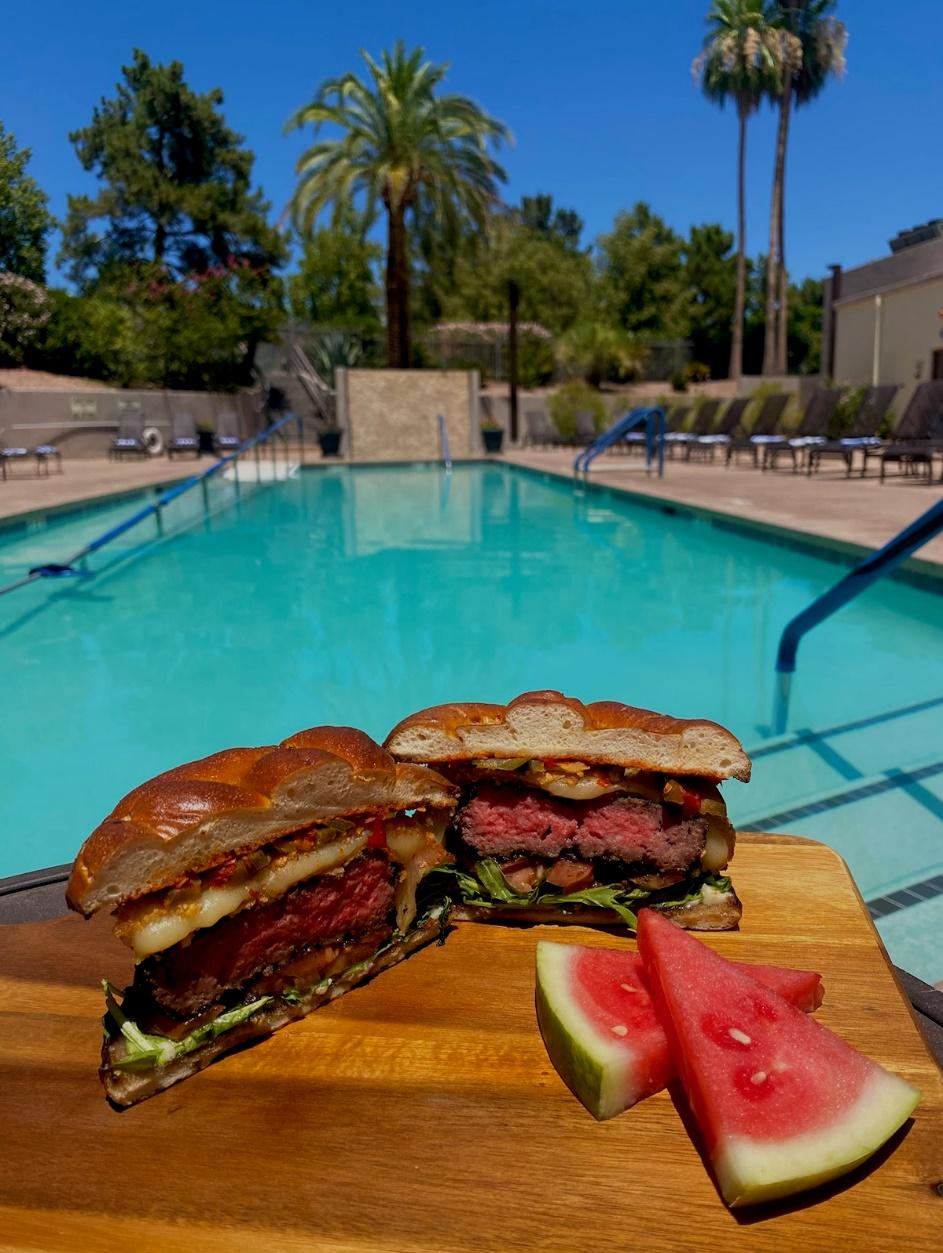 A sandwich and watermelon next to a pool

Description automatically generated