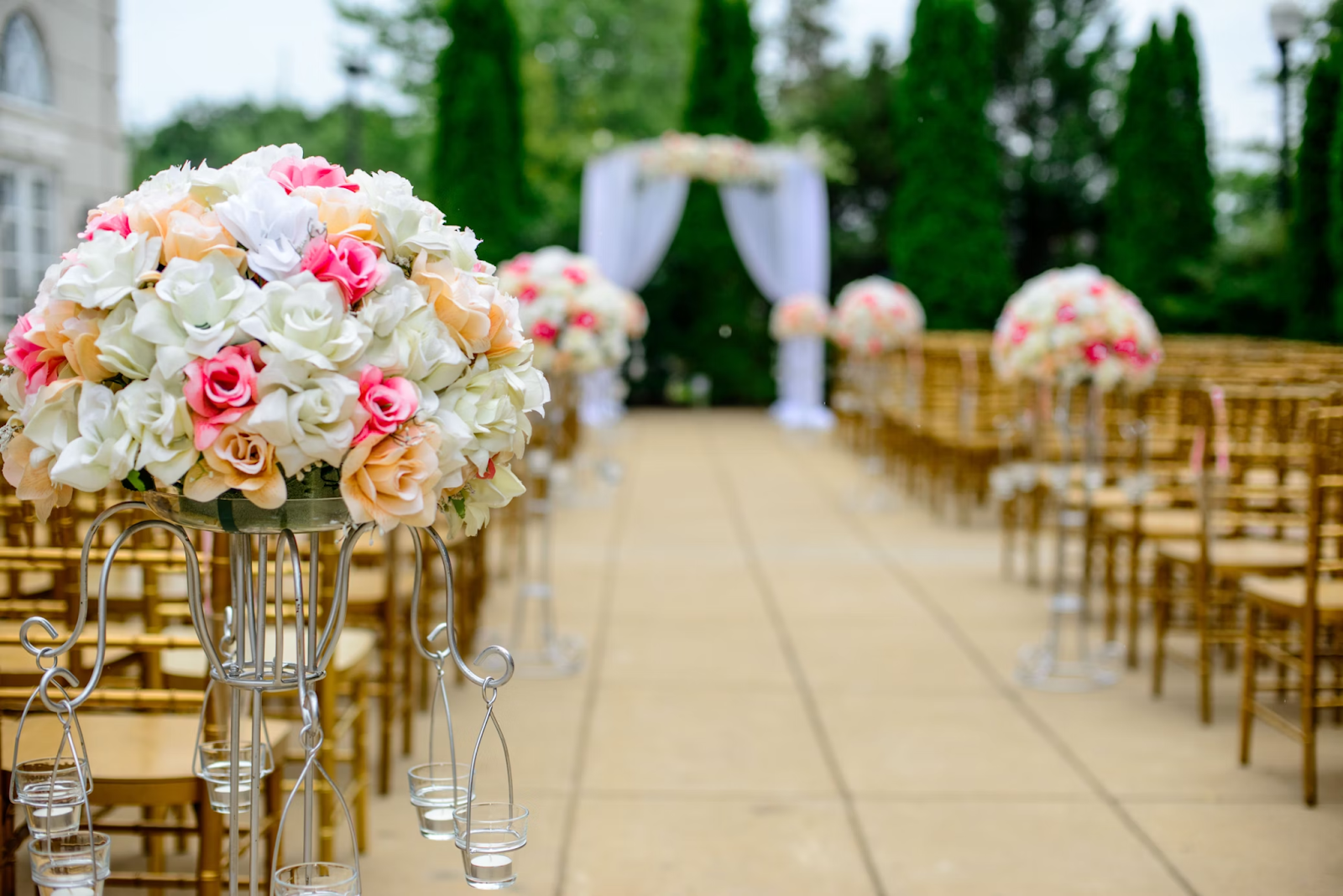 picture of an outdoor wedding venue lined with wooden chairs, with a colorful bouquet of white, pink, and peach roses in the foreground