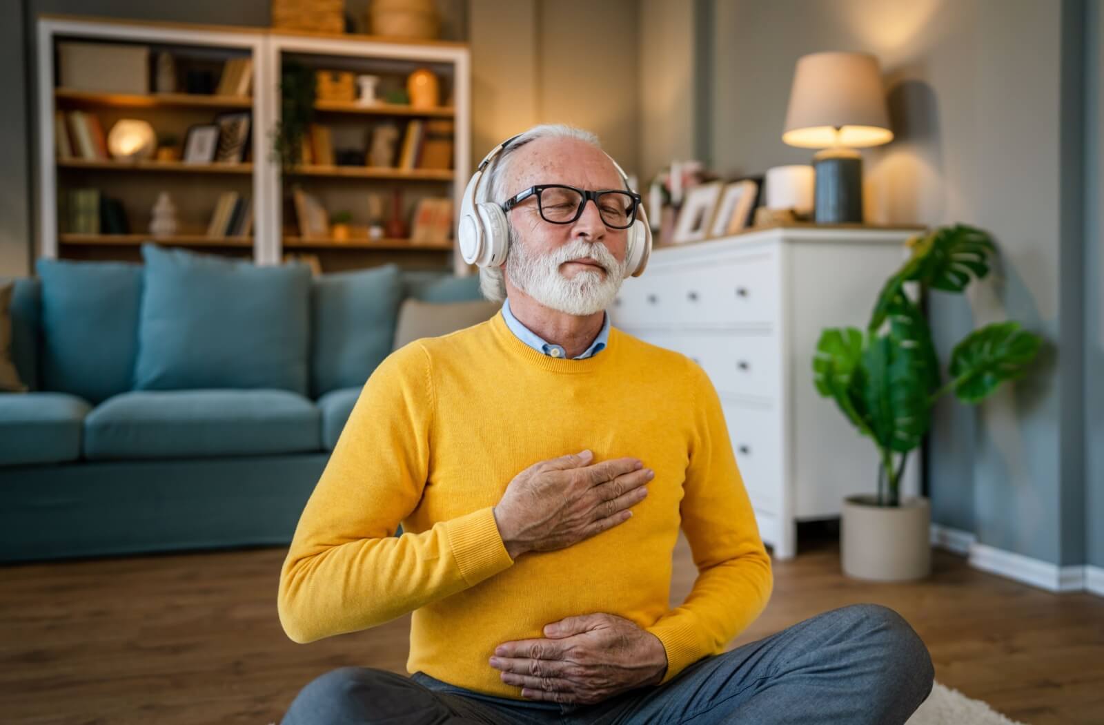 An older adult man using headphones for online guided meditation.