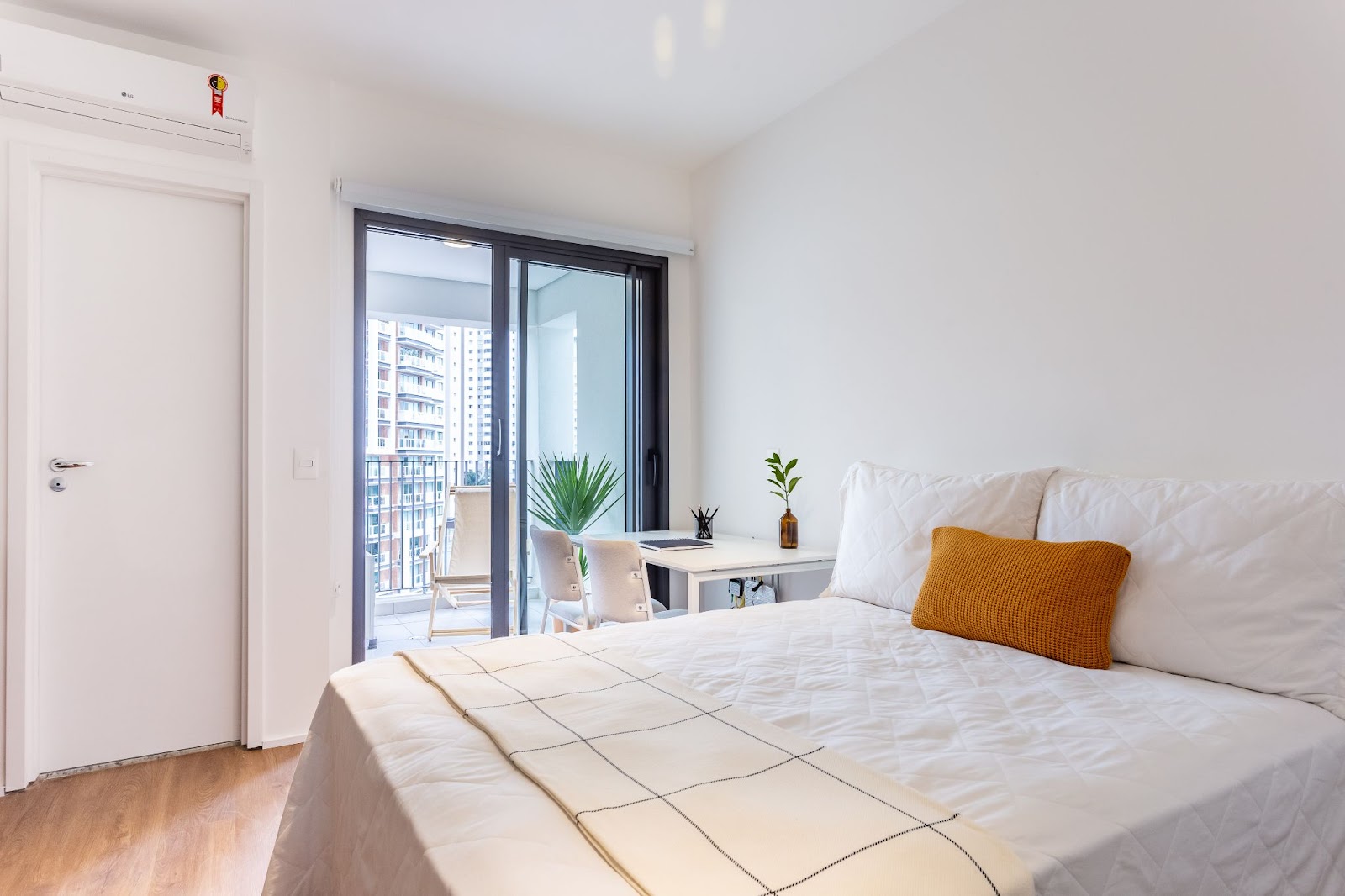 Foto de um quarto todo branco em um dos imóveis para investimento, com uma cama de casal, uma mesinha de canto e uma varanda.