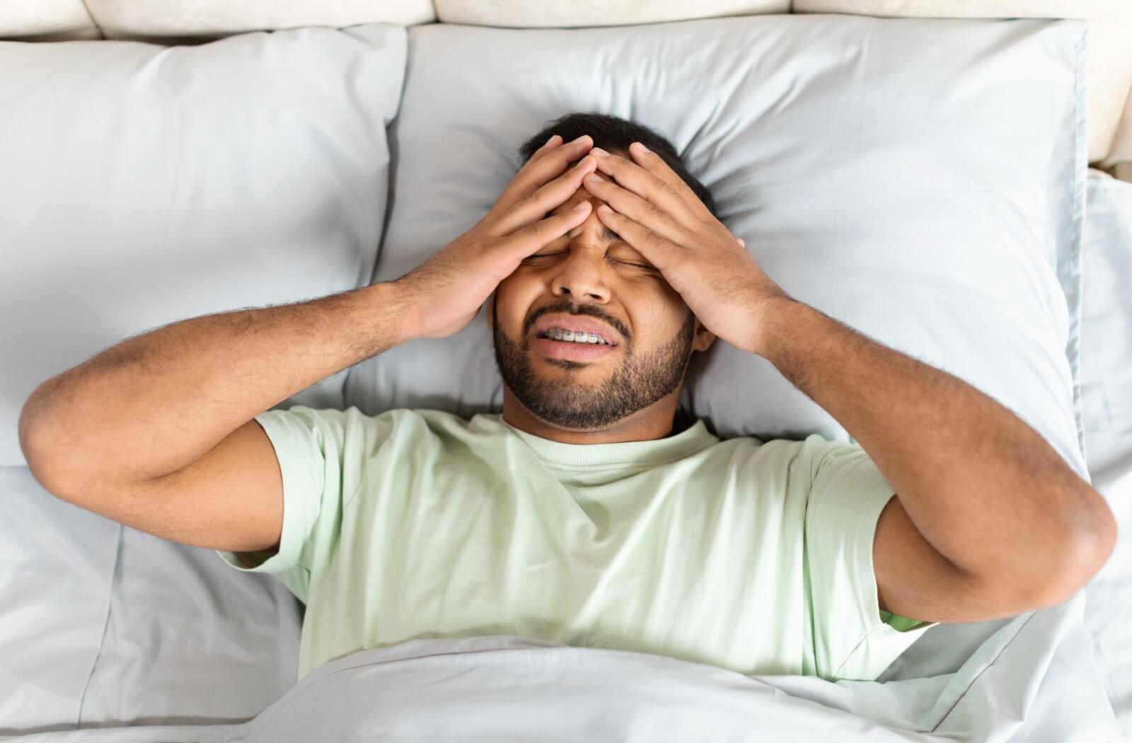 A man, who is experiencing a headache, rubbing his head and grimacing.
