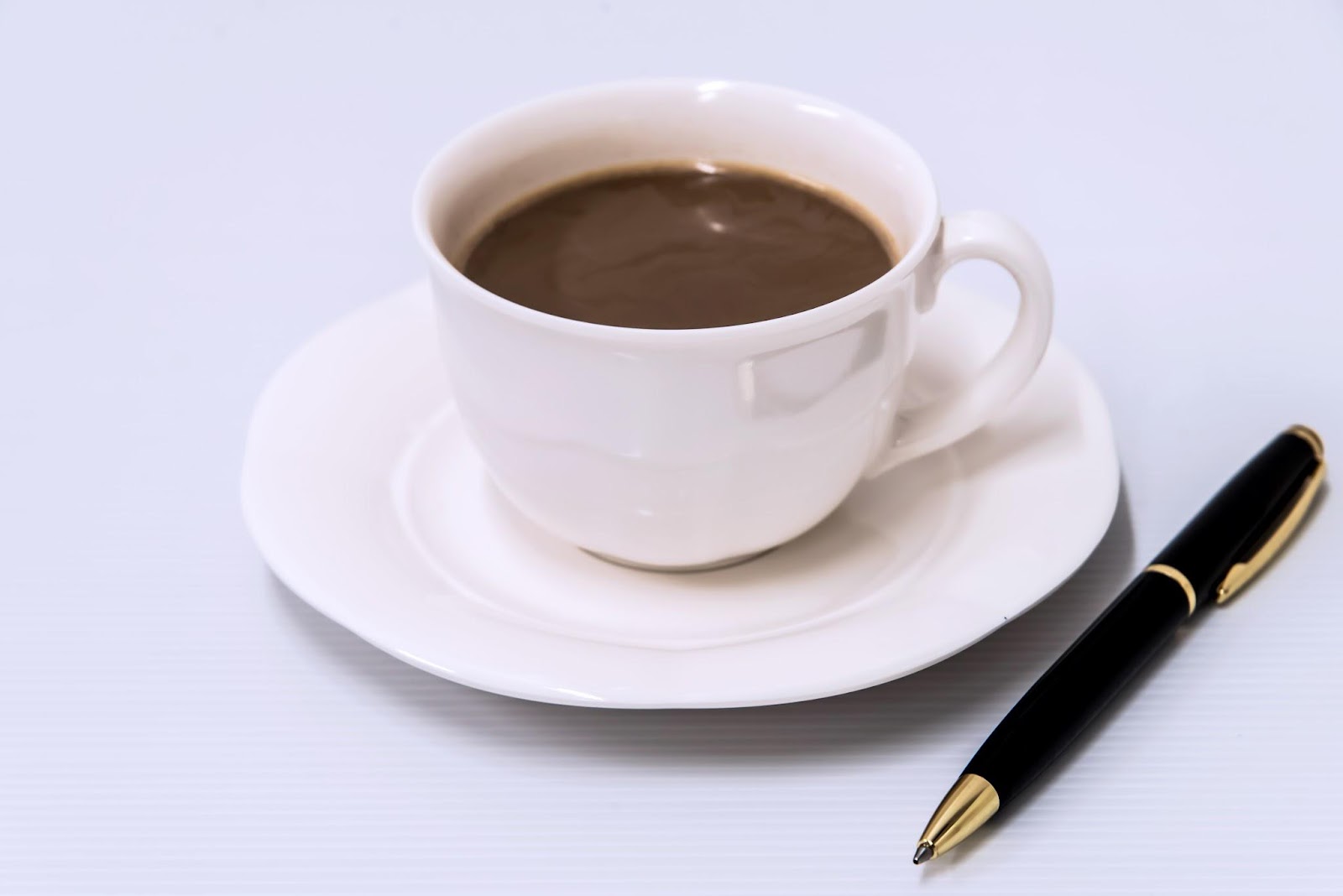 ボールペンが右側においてある、白いカップに入ったコーヒーの画像です。