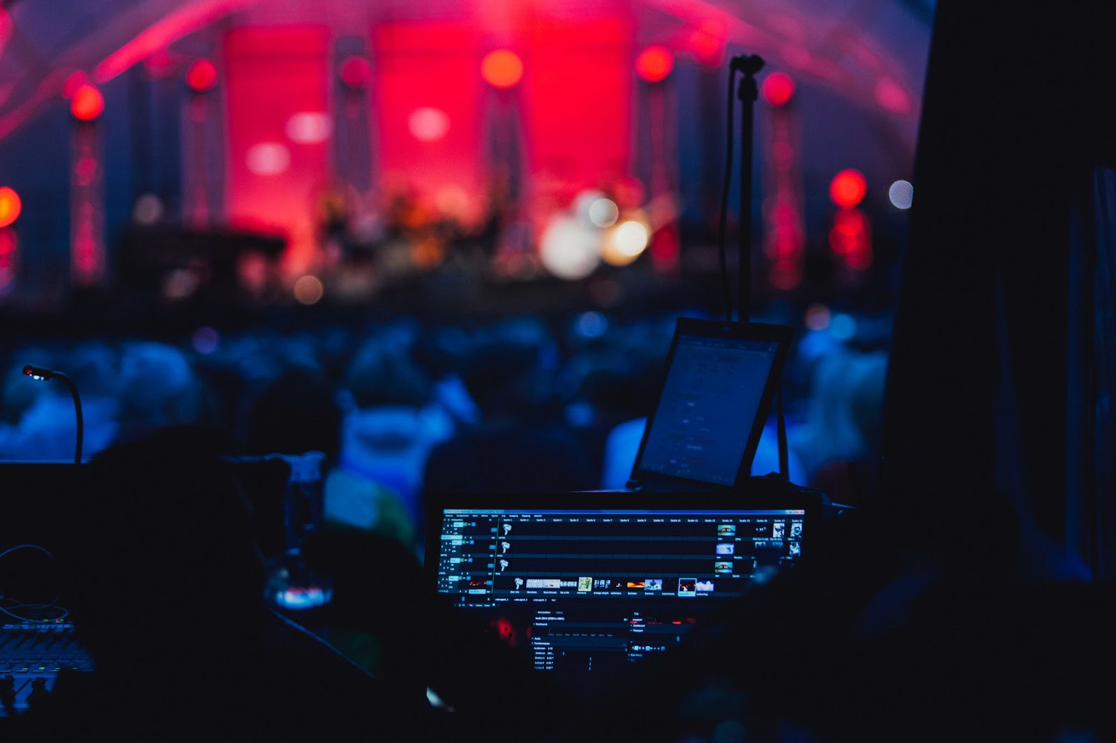 View from behind a DJ booth overlooking a concert crowd with stage lights illuminating the audience in a captivating blue hue.