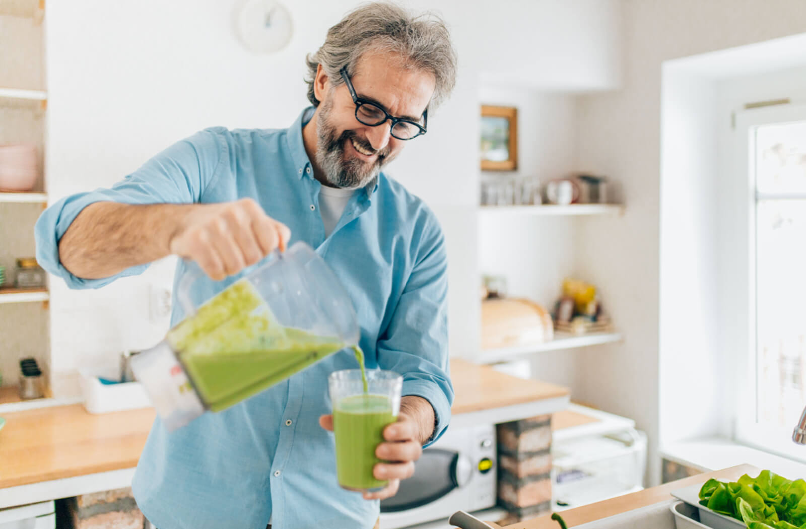 An older adult man pouring a freshly made smoothie from a blender to his glass.