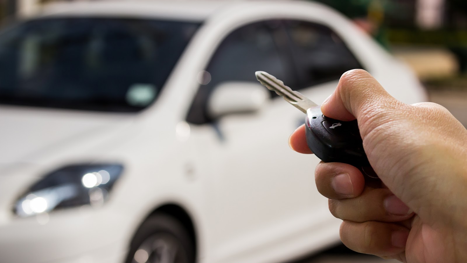 A user pressing a button on the remote car key. A car is seen in the background