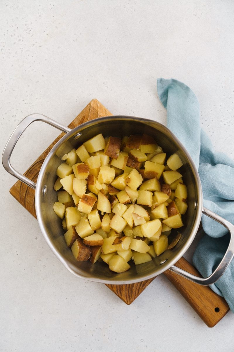 Sliced red skin potatoes in a pan on a wooden cutting board.