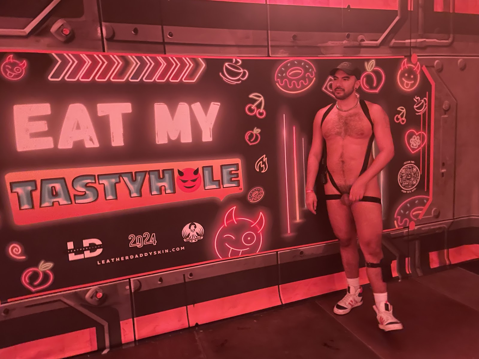 gay onlyfans content creator Phil standing in a gay fetish outfit beside a taste my tastyhole sign in darklands 2024 event party