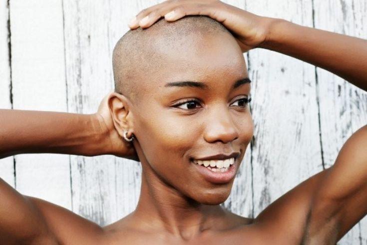 A girl with her hands on her bald head, smiling. 