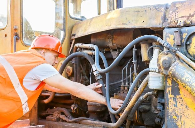 Photo working man in helmet examining bulldozer engine