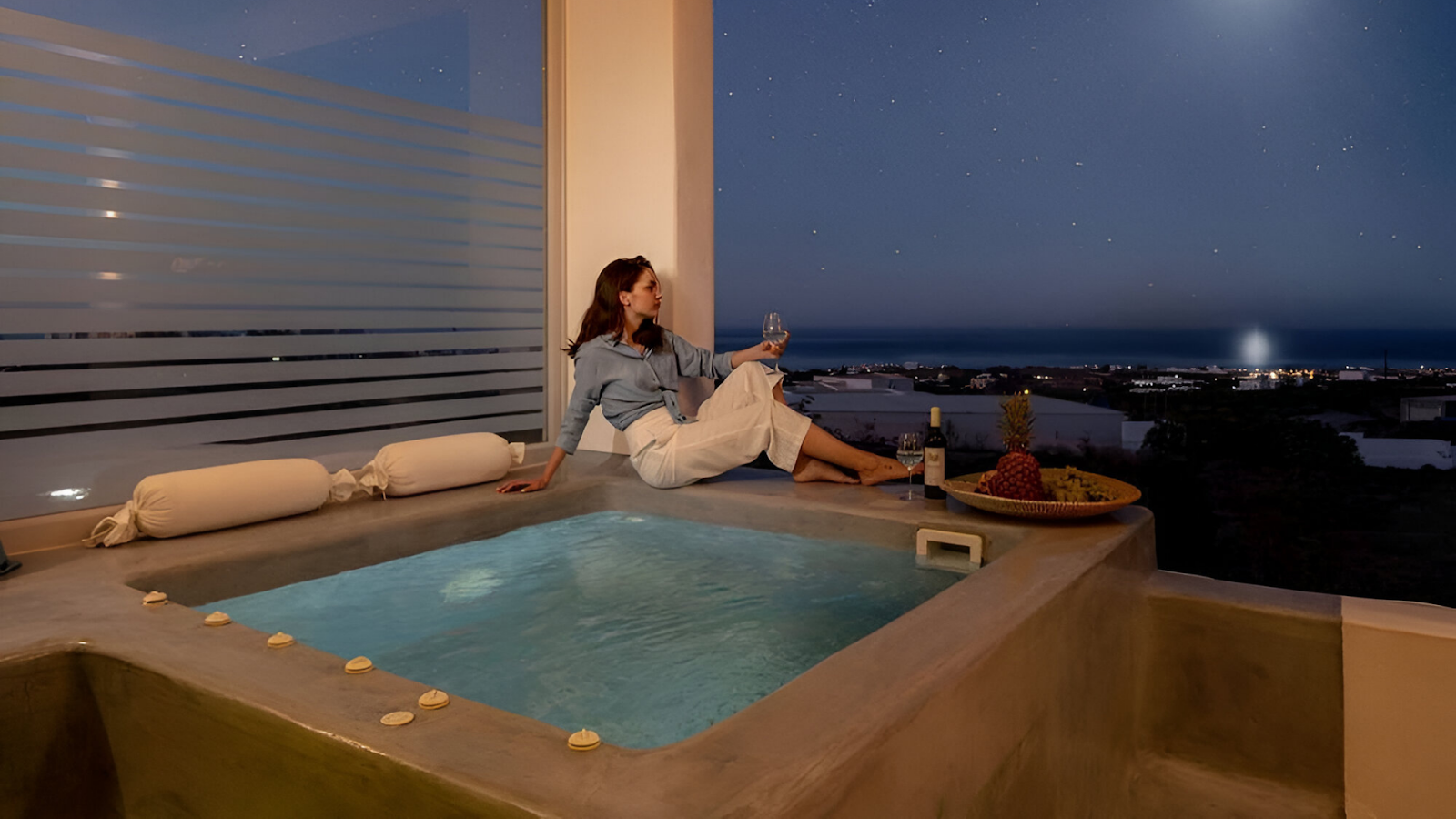 A woman holding a glass of wine beside a jacuzzi of a vacation rental in Santorini
