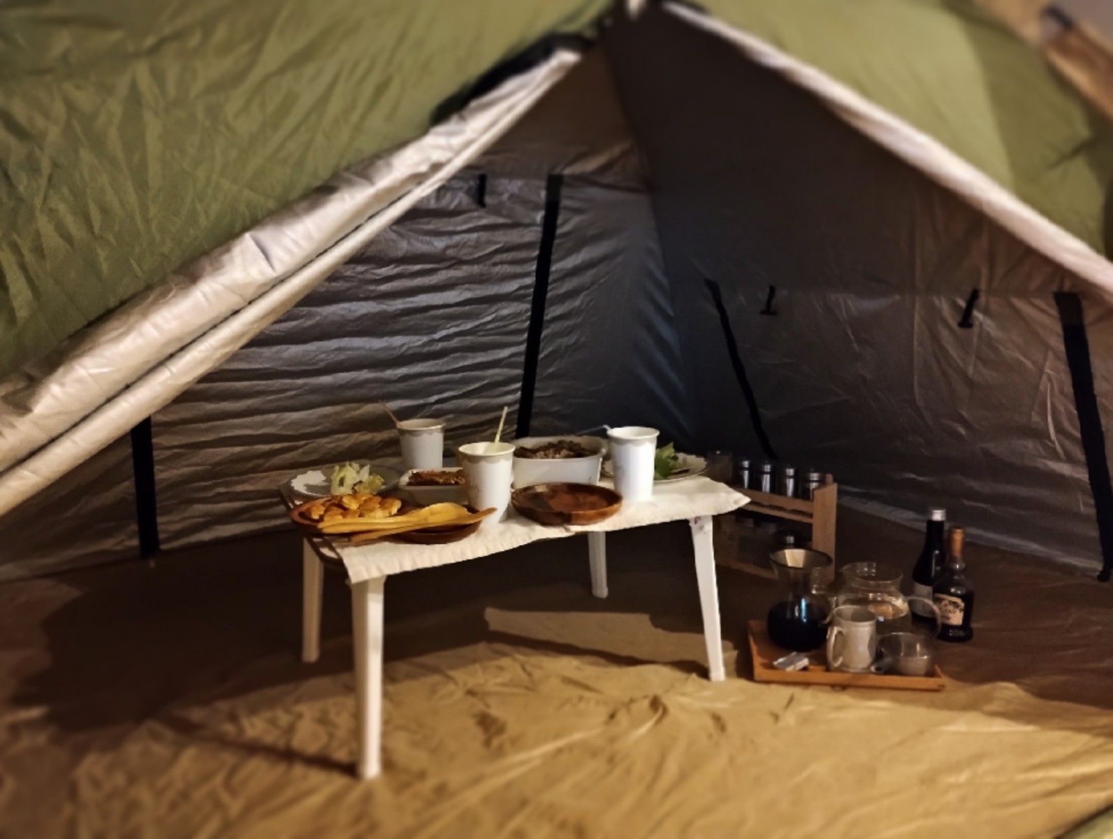 キャンプ用テントの中に、小さなテーブルとお盆が置いてあり、食べ物や飲み物が並べられている様子