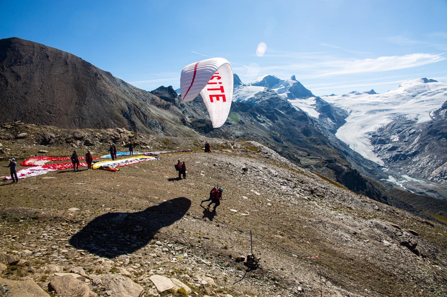 A group of people flying a parachute over a mountain

Description automatically generated