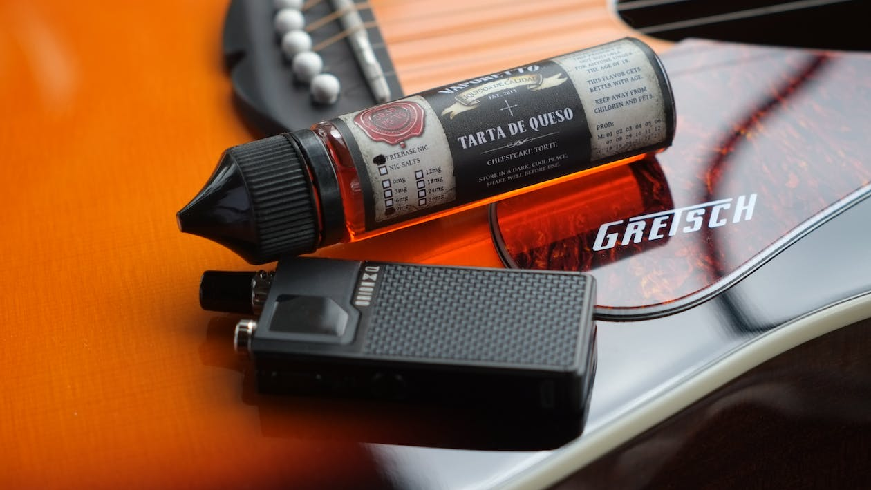 Free Vape and Cheesecake Flavored Liquid Cartridge Lying on a Guitar Stock Photo